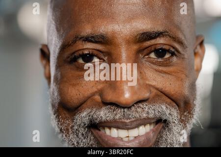 Homme afro-américain senior souriant largement tout en posant au studio avec un éclairage diffus. Portrait, senior, bien-être, confiance, digne, candide, Banque D'Images