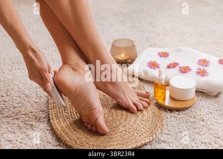 Femme utilisant la pierre ponce sur les talons pour l'élimination des callosités et les pieds mous, pédicure à la maison et soins de spa avec de la crème et de l'huile pour une peau lisse Banque D'Images