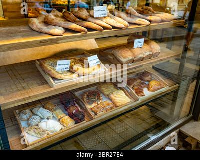 Assortiment de produits de boulangerie et de pâtisseries exposés derrière le verre dans une boulangerie, avec étiquettes de prix visibles. Usage éditorial exclusif. Aucune autorisation du modèle ou du propriétaire n'est disponible Banque D'Images