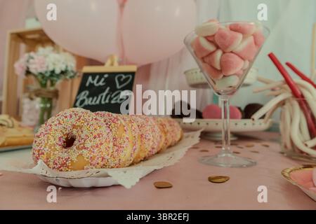 Gros plan sur une table festive à dessert sur le thème rose, avec une ligne de beignets glacés avec des pépites et un verre de guimauves en forme de cœur. Banque D'Images