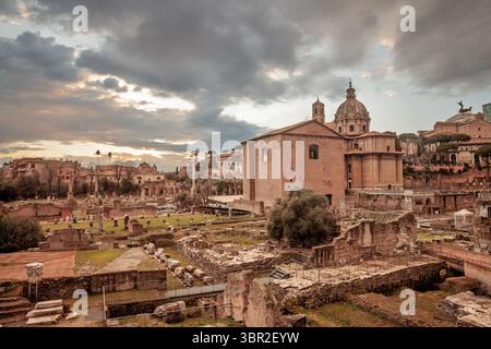 Panorama du Forum Romain (Foro romano) : colonnes en ruines, murs de basilique et le dôme baroque de Santi Luca e Martina s'élèvent contre les nuages couvrants au-dessus de t Banque D'Images