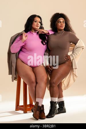 Diverses amies féminines posant en studio assis sur un tabouret portant des bottes de bodys Banque D'Images