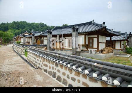 Gongju, Corée du Sud - 13 juin 2025 : une rangée de maisons d'hôtes hanok au toit en tuiles avec des cheminées et des piles de bois de chauffage bordent une ruelle aux murs de pierre à Gongju Hano Banque D'Images