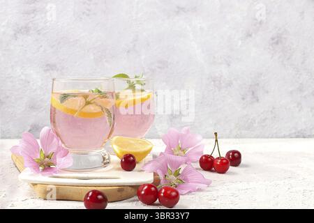 Thé glacé cerise ou cocktail de menthe et citron, une recette rafraîchissante de boisson estivale. Verre avec limonade aux fruits de pomme sur table en béton léger, régime de désintoxication et Banque D'Images