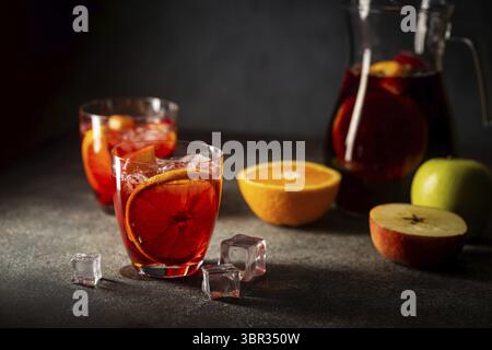 Vin rouge rafraîchissant sangria ou punch avec fruits frais dans des verres et pincher sur fond noir Banque D'Images