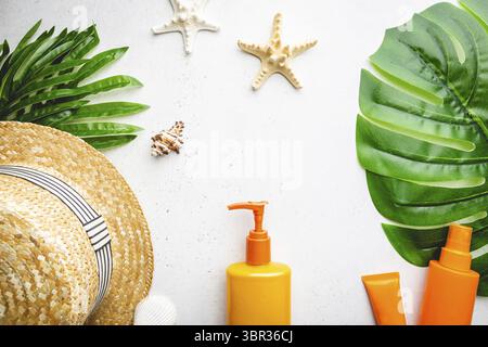Bouteilles de crème solaire disposées avec chapeau de paille sur fond blanc avec feuilles de palmier, vue du dessus Banque D'Images