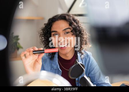 Créateur non binaire souriant et tenant l'applicateur de rouge à lèvres au bureau en studio avec microphone Banque D'Images