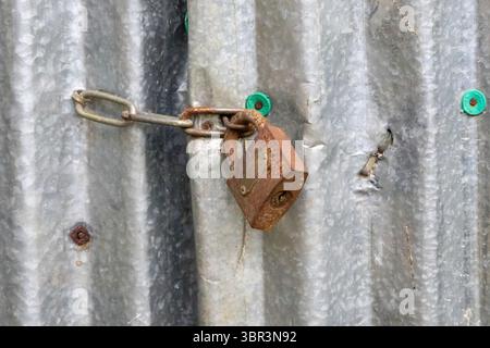Gros plan d'une vieille serrure rouillée et d'un maillon de chaîne sur une porte en tôle de fer galvanisé. Porte de maison de village dans le Bangladesh rural. Banque D'Images
