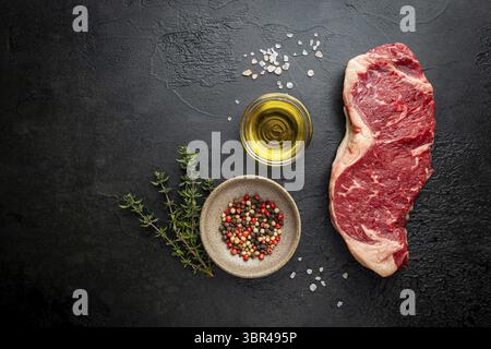 Viande fraîche crue bœuf de New York Steak sur fond noir, vue du dessus Banque D'Images