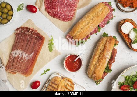 Assortiment de délicieux sandwichs baguettes remplis de jambon ou de salami finement tranché et de laitue verte fraîche ou roquette pour le petit déjeuner disposés sur dos blanc Banque D'Images