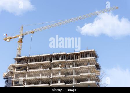 Grue de construction sur le fond d'un bâtiment inachevé et un ciel bleu avec des nuages Banque D'Images