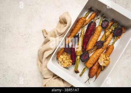 Jeunes carottes entières colorées rôties aux herbes servies sur une plaque de cuisson sur fond blanc. Vue de dessus Banque D'Images