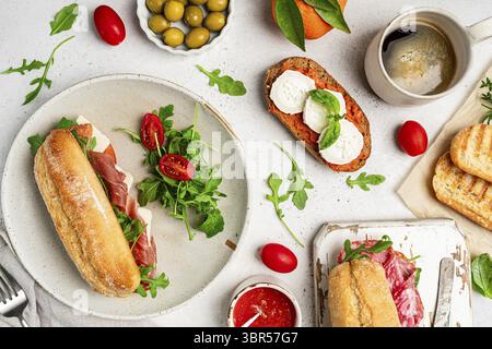 Assortiment de délicieux sandwichs baguettes remplis de jambon ou de salami finement tranché et de laitue verte fraîche ou roquette pour le petit déjeuner disposés sur dos blanc Banque D'Images