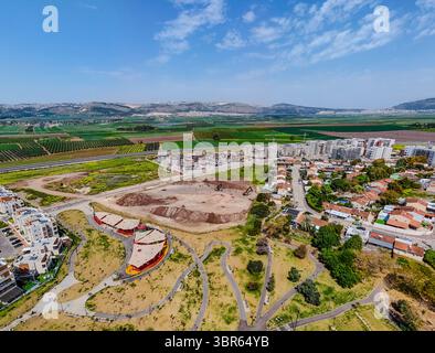 Vue aérienne des champs verdoyants rencontrent des logements modernes, contrastant avec les collines arides au loin, Afula, North District, Israël. Banque D'Images