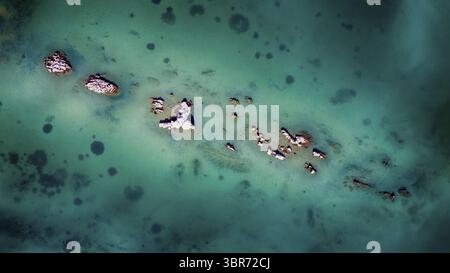 Vue aérienne de rochers accidentés ponctuent l'étendue turquoise de la mer Adriatique, une danse de textures et de tons, Split, comté de Split-Dalmatie, Croatie. Banque D'Images