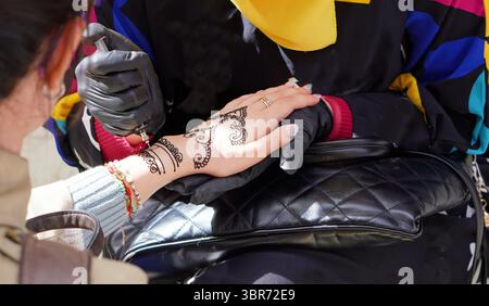 Gros plan d'une femme en hijab dessinant un dessin détaillé de mandala au henné sur la main d'un touriste à l'extérieur. Banque D'Images
