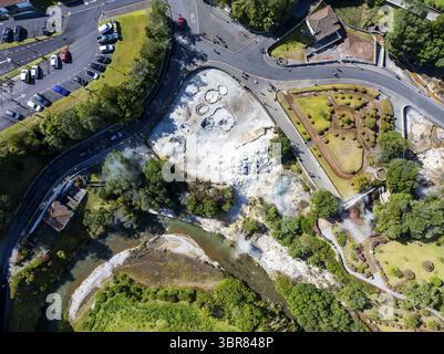 Vue aérienne de champs géothermiques bouillonnant de vapeur près d'une rivière sinueuse, à côté de jardins et de routes entretenus, une tapisserie de la nature et des humains Banque D'Images