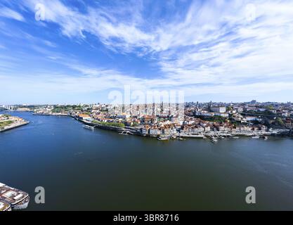 Vue aérienne du fleuve Douro serpentant à travers la ville, reflétant le ciel Azur ci-dessus, avec le pont Dom Luís I au loin, Porto, Porto District, Portugal. Banque D'Images