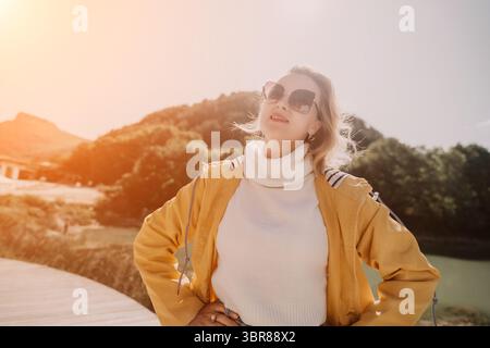 Femme, lunettes de soleil, montagne. Femme heureuse en lunettes de soleil posant devant les montagnes un jour ensoleillé. Banque D'Images