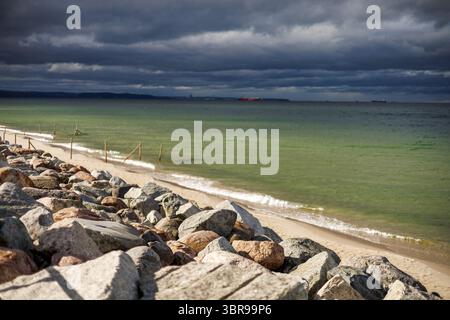 Une scène côtière spectaculaire avec de grands rochers sur une plage de sable, une mer verte calme et un ciel orageux. Banque D'Images