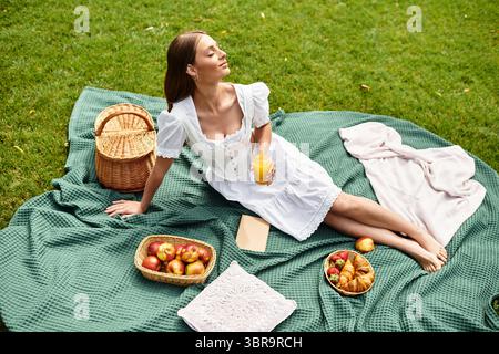 Une jeune femme se détend sur une couverture de pique-nique, dégustant un verre et de savoureux collations. Banque D'Images