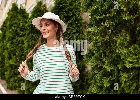 Jeune femme avec des tresses sourit joyeusement tout en ayant un pique-nique dans un cadre de parc luxuriant Banque D'Images