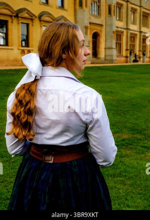 Une femme en vêtements d'époque se tient sur une pelouse devant un grand bâtiment. Banque D'Images