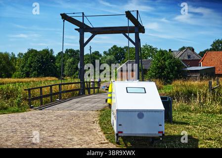 Caravane blanche garée sur une route de briques près d'un pont-levis surélevé aux pays-bas, offrant une vue pittoresque sur la vie rurale et les voyages durables Banque D'Images