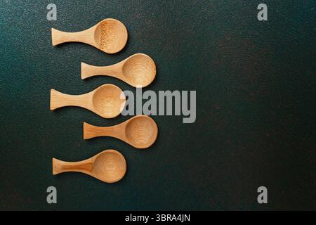 Cinq cuillères en bois de différentes tailles placées en rangée sur une surface sombre. Banque D'Images