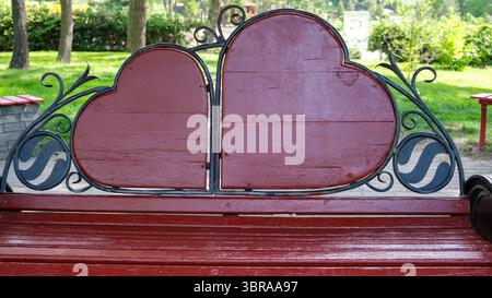 Couple profite d'un moment romantique assis sur un charmant banc à thème de coeur à l'extérieur. Banque D'Images