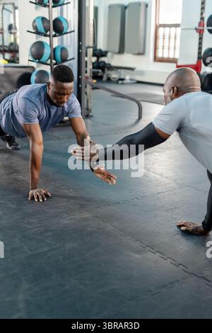 Entraîneur personnel afro-américain et client faisant des pompes et tapotant par rack de medicine ball au gymnase Banque D'Images