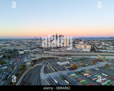 Vue aérienne des gratte-ciels du centre-ville perçant l'horizon, juxtaposés contre le port tentaculaire et les chemins de fer, le tout baigné dans les teintes douces de l'aube, Los Angeles, Californie, États-Unis. Banque D'Images