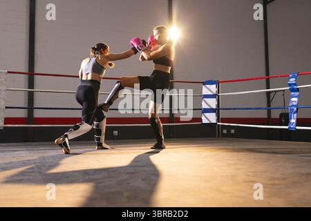 Deux boxeurs féminins portant des gants et des protège-tibias battant sous la lumière du soleil dans l'anneau avec des cordes Banque D'Images