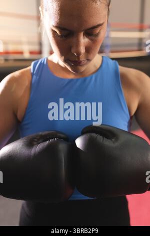 Boxer féminin amenant des gants noirs ensemble à la poitrine à l'intérieur de l'anneau avec des cordes dans le débardeur bleu Banque D'Images