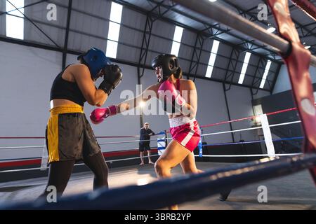 Deux femmes boxeurs sparring avec coiffure échangeant des coups de poing dans un ring de boxe tout en observant l'entraîneur Banque D'Images