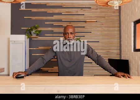 Homme afro-américain debout derrière le comptoir de réception en bois clair dans le hall tenant un dispositif de carte Banque D'Images