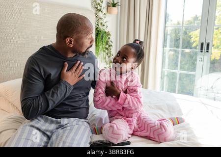 Père afro-américain et fille pratiquant la respiration sur le lit à côté du smartphone et de la brosse à cheveux Banque D'Images