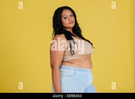 Femme debout dans le profil contre fond de studio jaune portant soutien-gorge de sport et leggings Banque D'Images