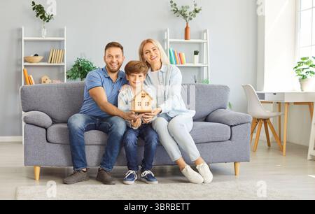 Famille célébrant l'achat d'une nouvelle maison tenant le modèle de maison en bois avec enfant Banque D'Images