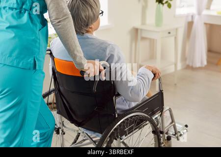 Femme âgée handicapée en fauteuil roulant assistée par une infirmière méconnaissable Banque D'Images