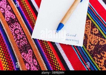 Tasse à café avec une note disant bonjour sur une table colorée avec tissage Inca. Banque D'Images