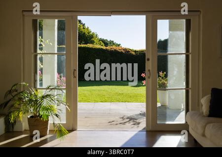 Portes vitrées coulissantes ouvrant large et révélant une terrasse en bois avec pelouse verte sous la lumière du soleil Banque D'Images