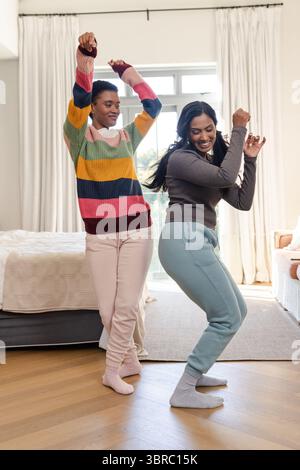 Diverses amies féminines dansant sur plancher de bois franc dans la chambre à coucher par une grande fenêtre et des rideaux blancs Banque D'Images