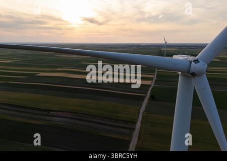Vue aérienne d'une éolienne sur un champ agricole au coucher du soleil. Gros plan des lames. Banque D'Images