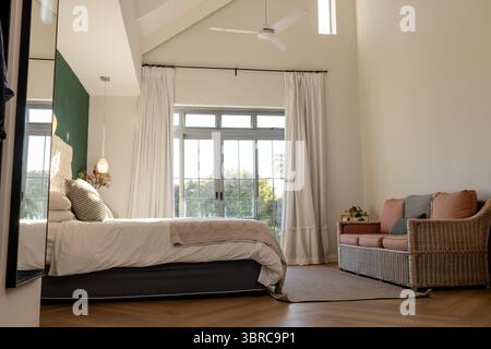 Chambre avec lit avec draps blancs et couverture à côté d'un canapé en osier et de plantes en pot Banque D'Images