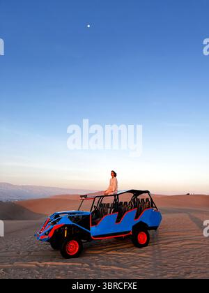 Femme assise sur le toit de buggy, qui conduit les touristes dans la zone désertique et regarder de beaux paysages arides Huacachina, ICA, Pérou Banque D'Images