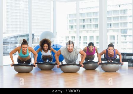 Cinq adultes effectuent des pompes sur des boules de bosu sur plancher de bois poli dans la scène de gymnastique plate Banque D'Images