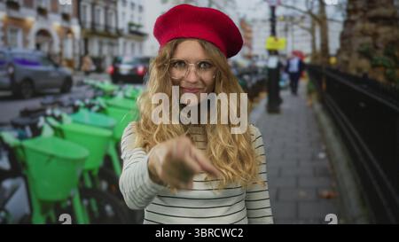 Femme utilise son doigt pour pointer la rue animée tandis qu'une jeune voyageuse blonde dans un béret rouge et des lunettes explore une scène urbaine. Banque D'Images