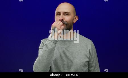 Des gestes d'homme chauve barbu sur fond bleu portant un pull gris exsudant charme et confiance. Banque D'Images