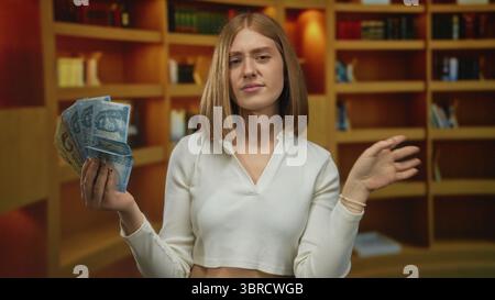 Jeune femme blonde tient fan de billets de banque hongrois en forint et lève son autre main la paume vers l'avant dans la bibliothèque ; hésitation de rejet. Banque D'Images